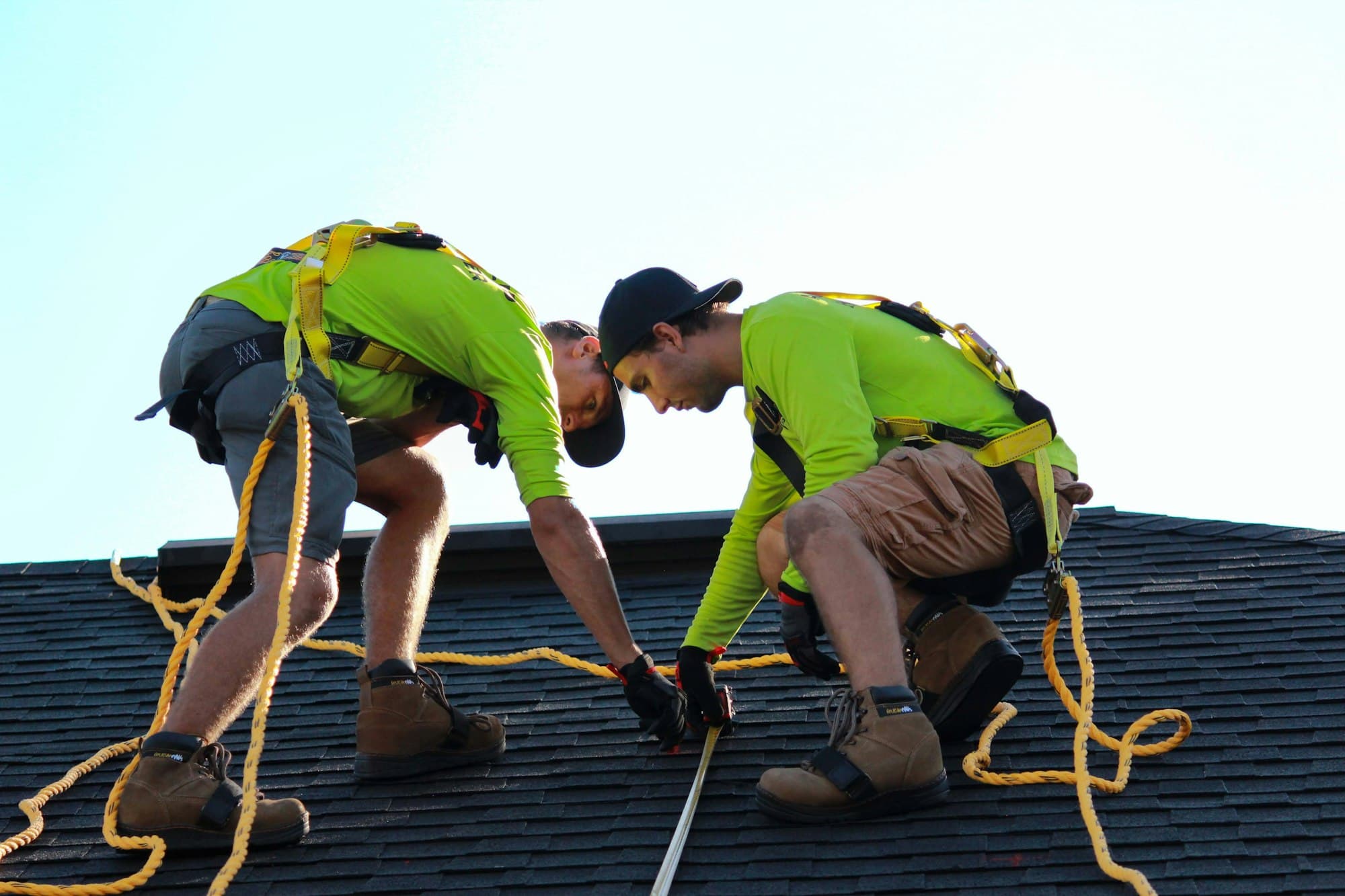 Roofing crew in high-visibility gear working a dark shingle roof